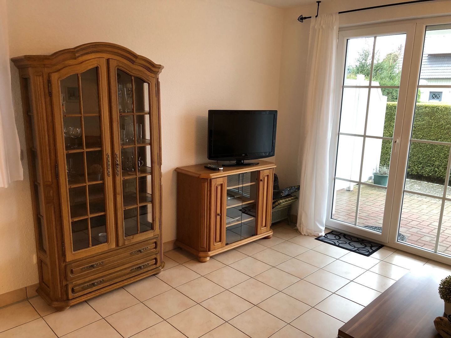A living room with a wooden cabinet, a television on a stand, and a sliding glass door leading to an outdoor area.