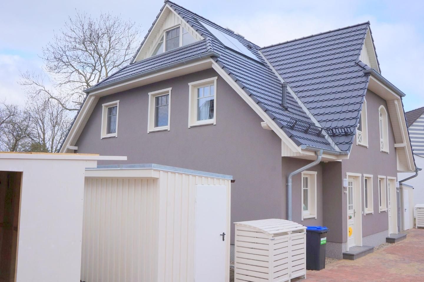 Een woonhuis met een grijze gevel, een schuin dak en een witte garage.