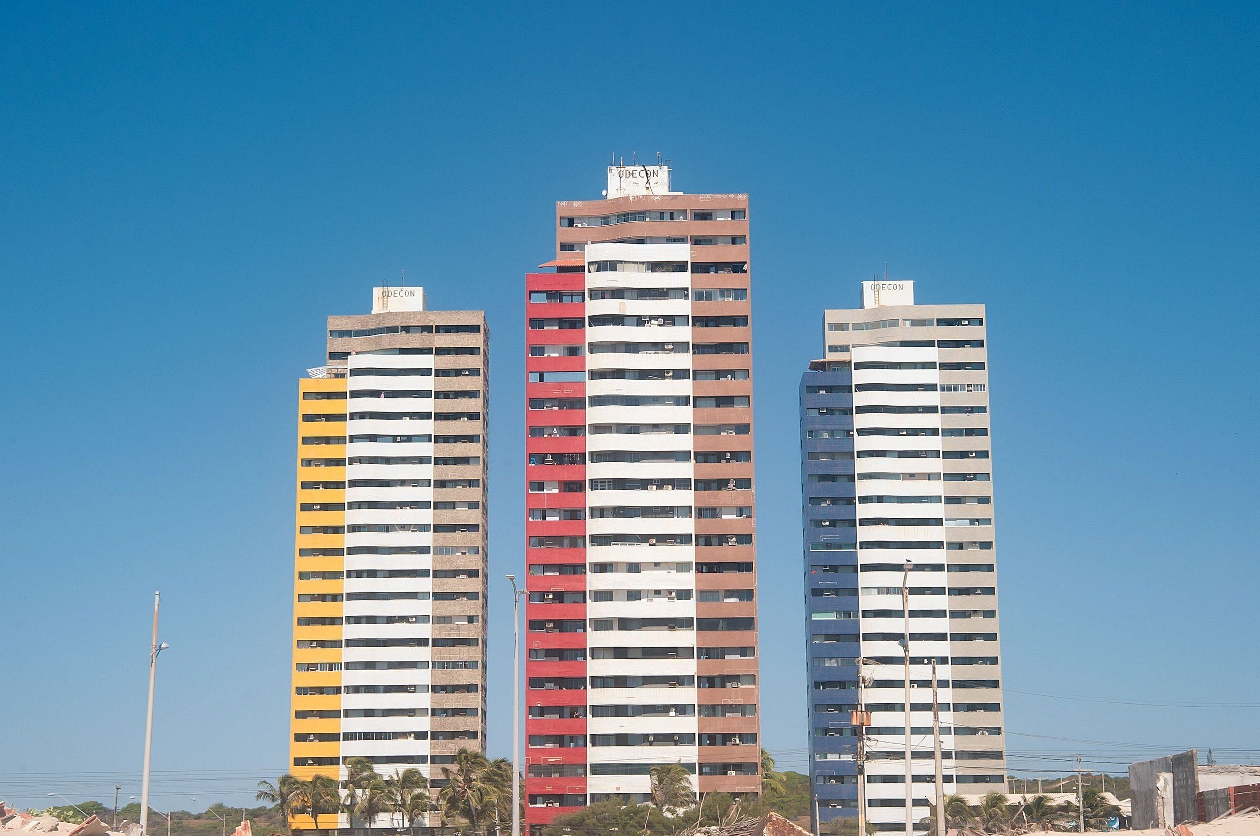 Three high-rise buildings with balconies, under a clear blue sky.