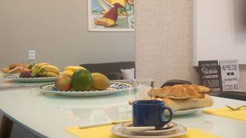 Disposição para o pequeno-almoço com pratos de fruta, um croissant e uma chávena azul sobre uma mesa com guardanapos amarelos.