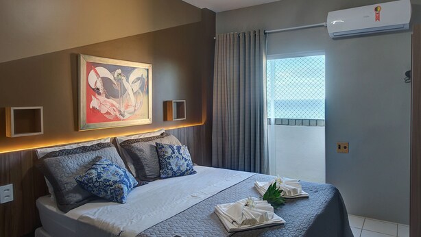 Habitación de hotel con cama, un cuadro, equipo de aire acondicionado y una ventana con cortinas.