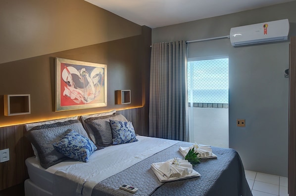 Quarto de hotel com cama, um quadro, ar condicionado e janela com cortinas.