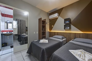 Quarto de hotel com duas camas, banheiro com pia e espelho.