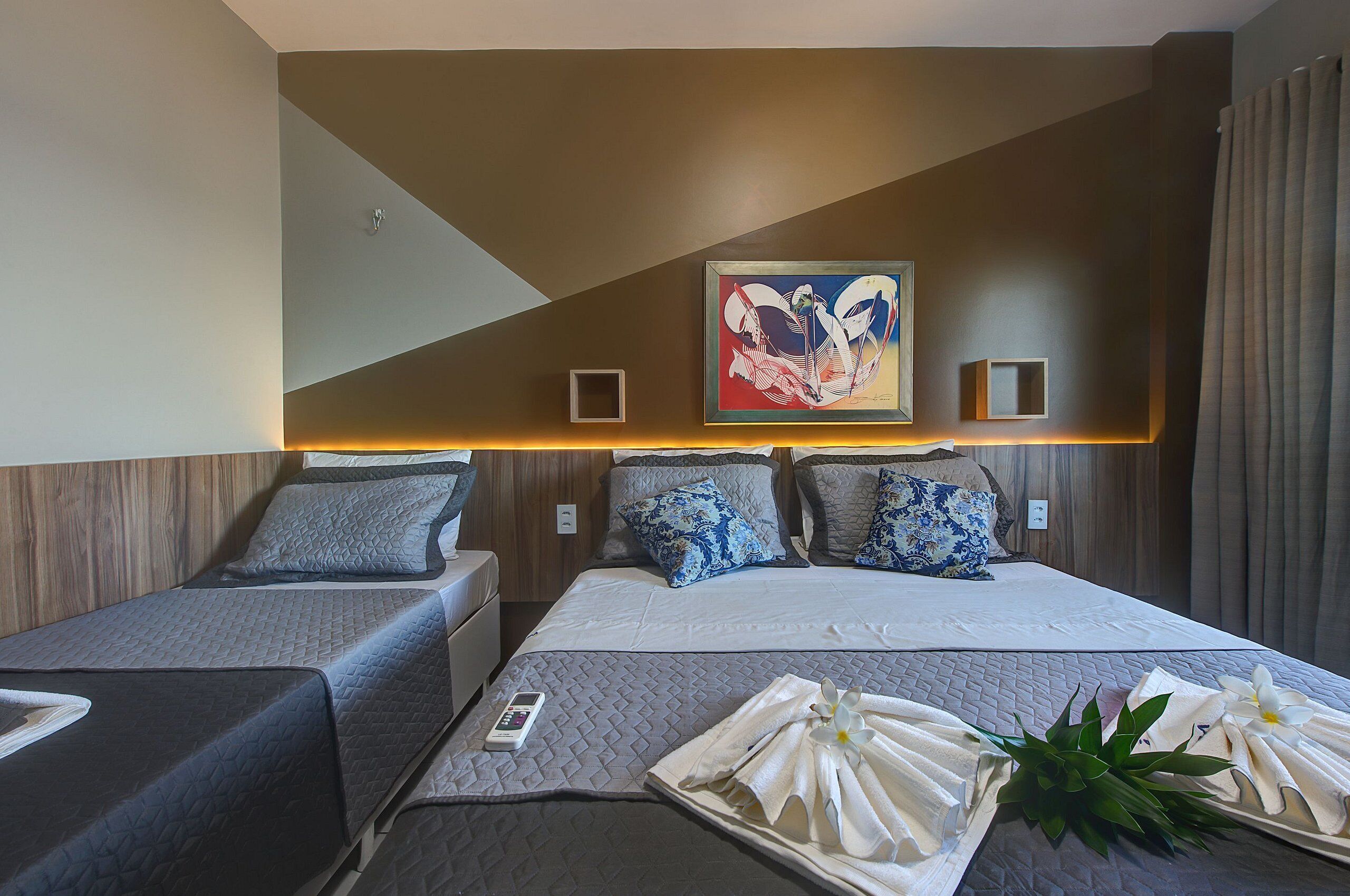 A hotel room with two beds, a painting on the wall, and a tray with towels and flowers on the bed.