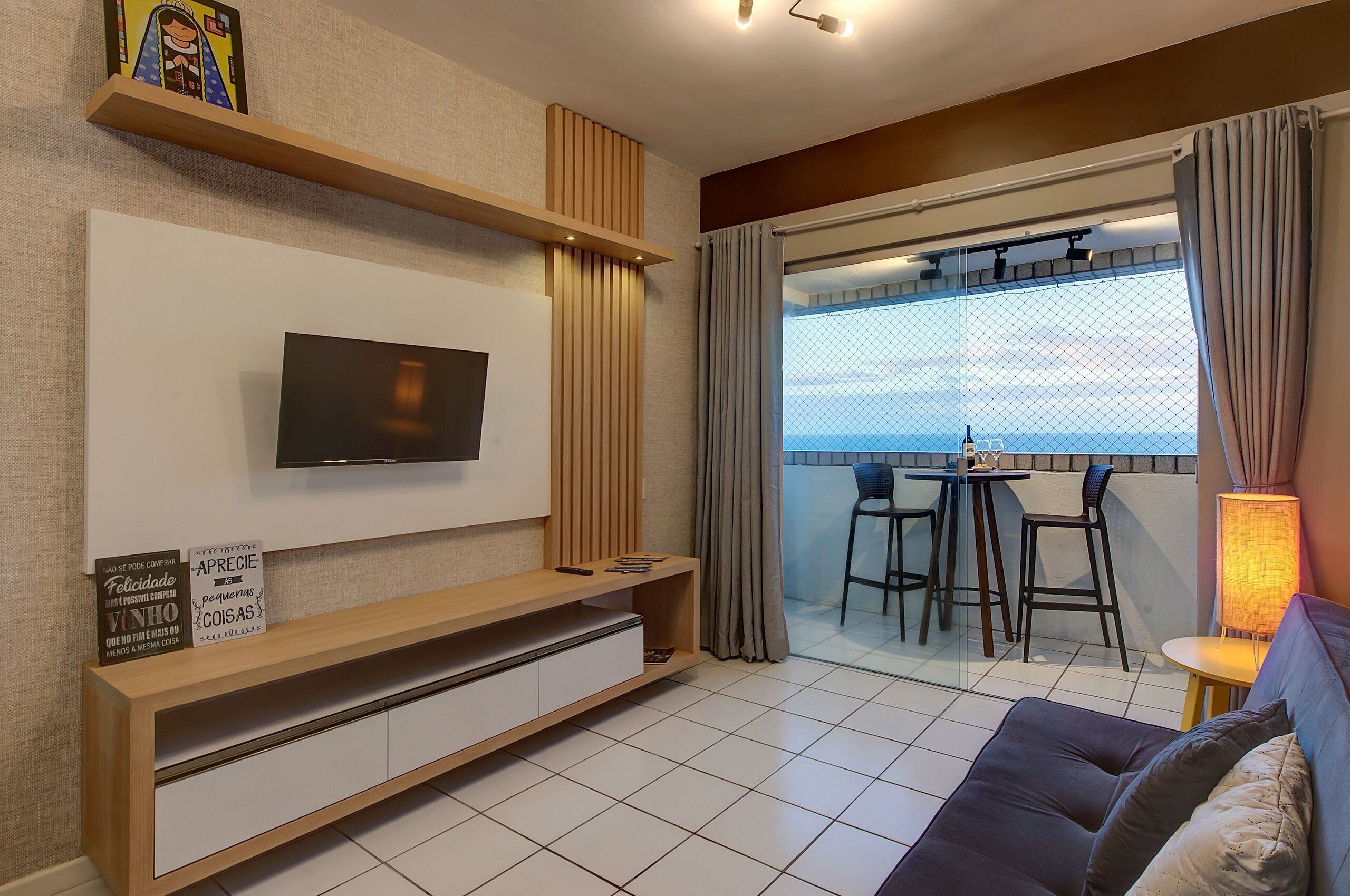 A modern living room with a flat-screen TV, a wooden console table, a dining area with a table and chairs, and a balcony with a view.