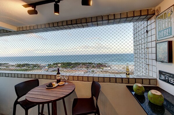 A balcony with a table set for two, a bottle of beer, and a plate of grapes.