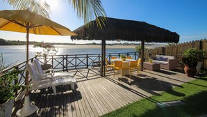 A wooden deck with a thatched roof, outdoor furniture, and a view of the water.
