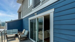 A blue house with a sliding glass door leading to a patio area with two wicker chairs and a small table.