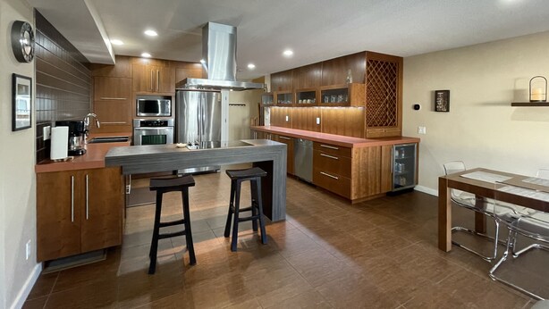 A modern kitchen with wooden cabinets, stainless steel appliances, and a central island with stools.