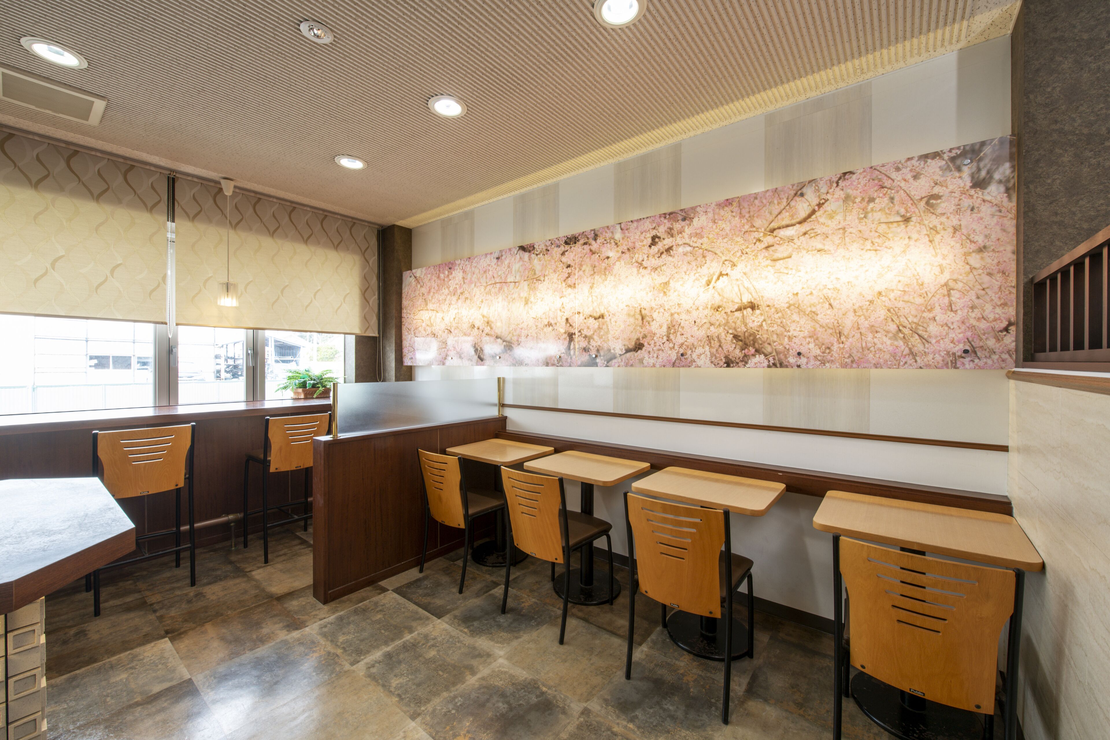 A restaurant with wooden tables and chairs, a large decorative wall, and a window with a view.