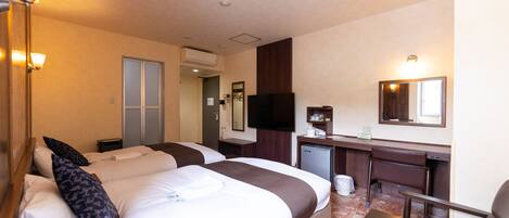 A hotel room with two beds, a desk, a chair, a television, and a small kitchenette.