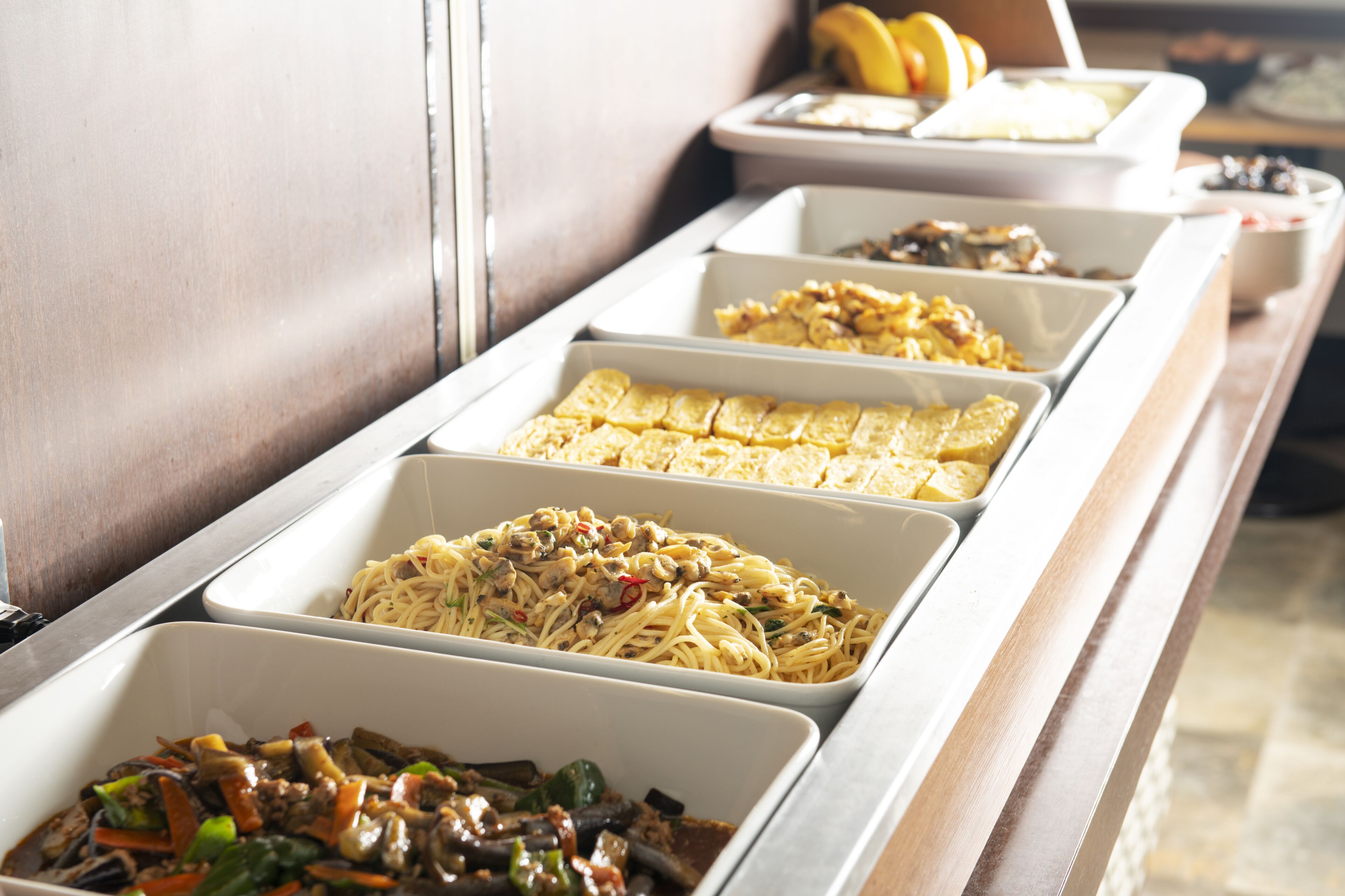Um buffet com diversos pratos, incluindo massa, macarrão e legumes refogados.