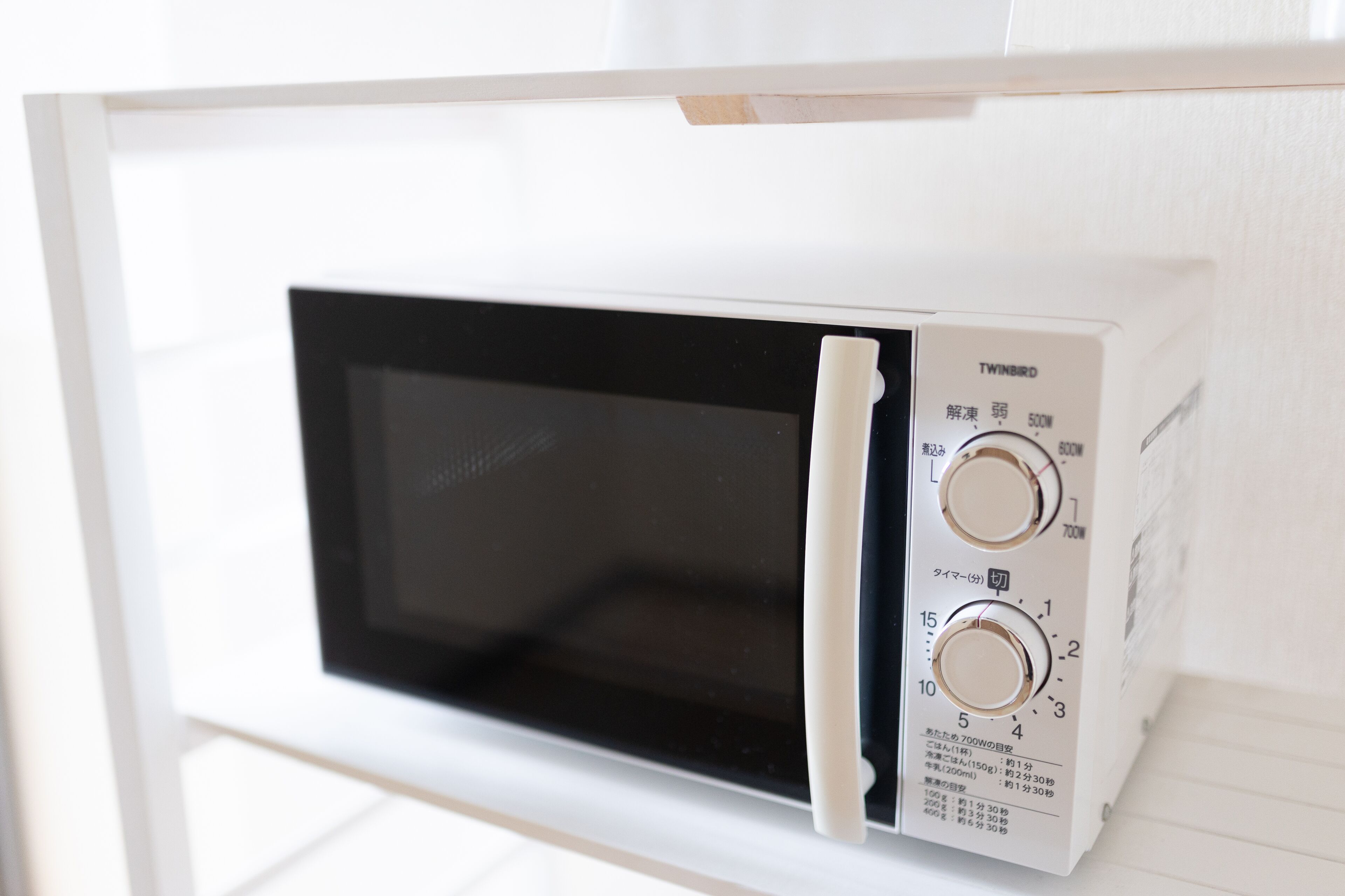 A white microwave with two dials and a black screen, mounted on a white shelf.