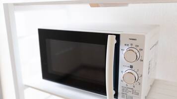 A white microwave with two dials and a black screen, mounted on a white shelf.