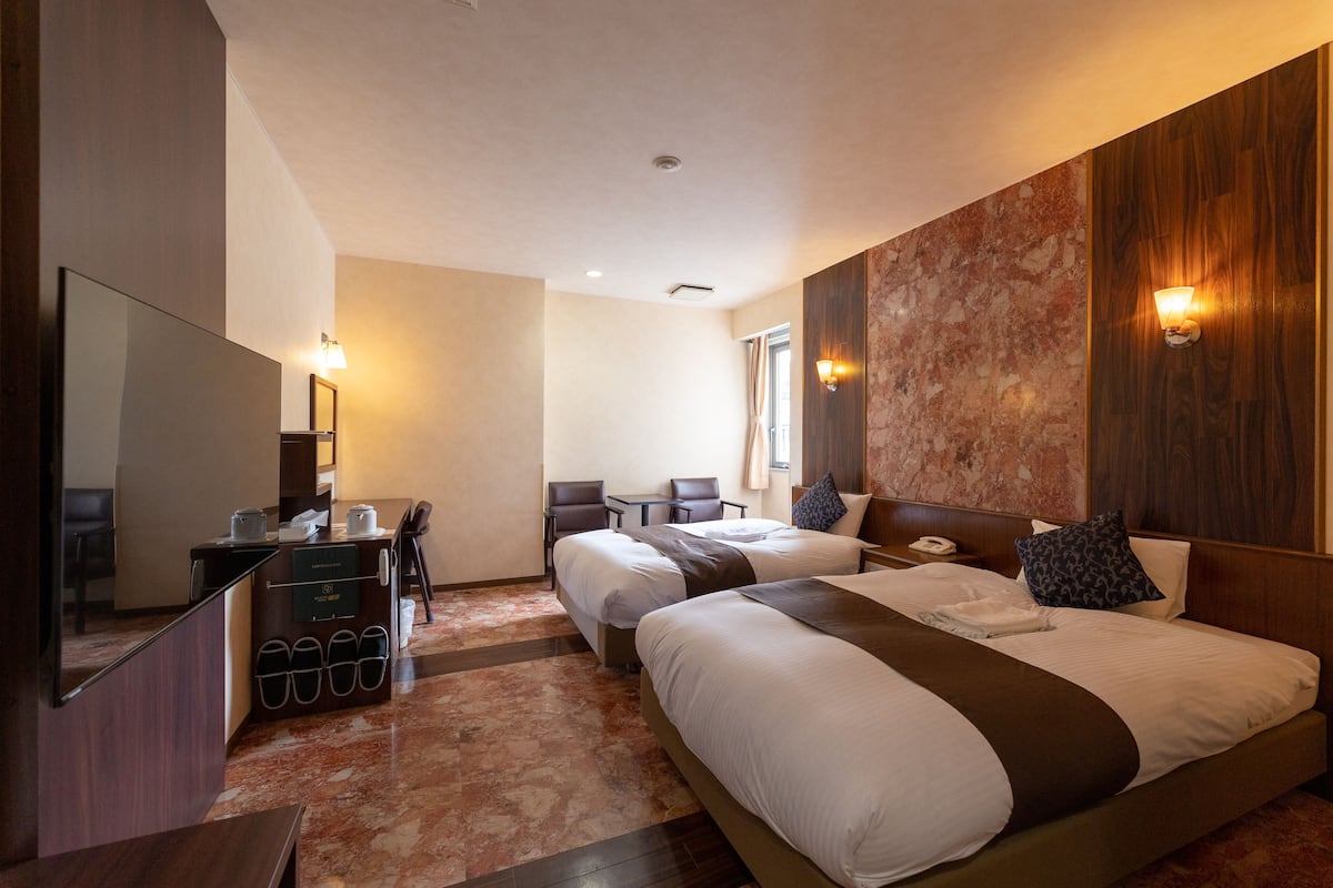Une chambre d’hôtel avec deux lits, un bureau avec une chaise, une petite table et un miroir.