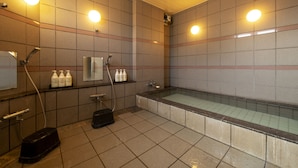 Moderni kylpyhuone, jossa on kylpyamme, suihku ja wc. Hyllyllä on pulloja erilaisia hygieniatuotteita.