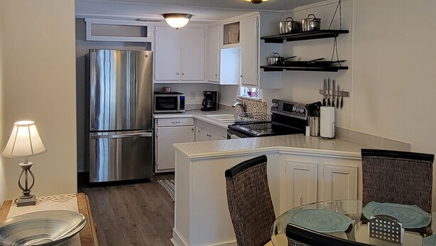 A modern kitchen with stainless steel appliances, a dining area with wicker chairs, and a central island. - Beach Cottage - family and pet friendly, beach access less than 100ft away (Fernandina Beach)