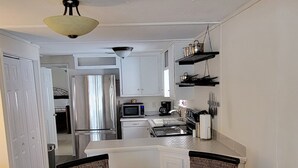 A modern kitchen with white cabinets, a microwave, and a coffee maker. There is a dining area with a glass table and wicker chairs. - Beach Cottage - family and pet friendly, beach access less than 100ft away (Fernandina Beach)