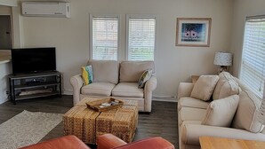 A living room with two sofas, a coffee table, a TV, and a lamp. - Beach Cottage - family and pet friendly, beach access less than 100ft away (Fernandina Beach)
