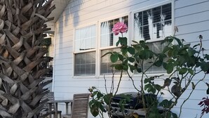 A white house with two windows, a wooden chair, and a grill in the backyard. - Beach Cottage - family and pet friendly, beach access less than 100ft away (Fernandina Beach)