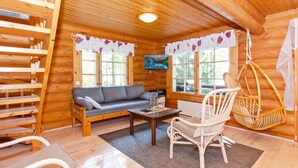 A cozy log cabin interior with a sofa, a hanging chair, a dining table, and a bookshelf. - Suvituuli by Interhome (Liperi)