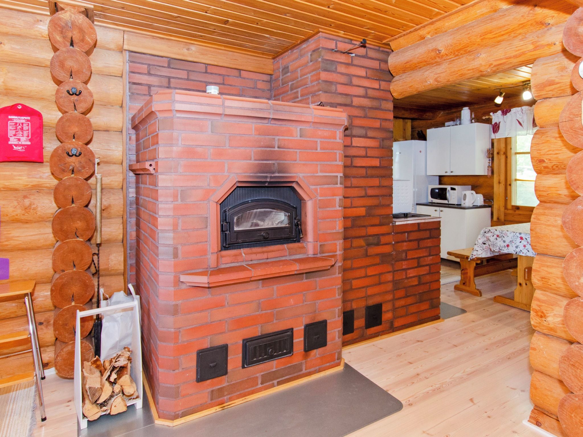 Une cheminée en briques avec un poêle à bois, un coin cuisine doté de meubles blancs et un intérieur en bois.