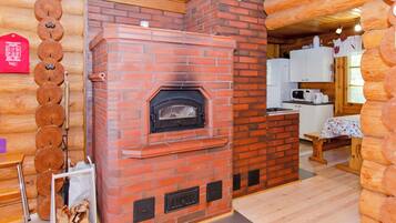 Une cheminée en briques avec un poêle à bois, un coin cuisine doté de meubles blancs et un intérieur en bois.