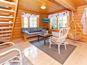 Een gezellig chaletinterieur met een bank, een eettafel, een hangstoel en een aan de muur bevestigde televisie.