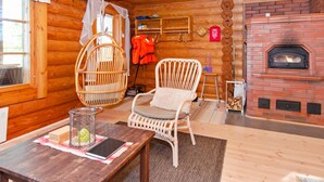 A cozy log cabin interior with a wooden table, wicker chairs, a hanging basket, and a brick fireplace. - Suvituuli by Interhome (Liperi)