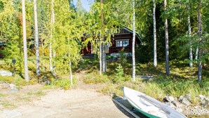 A cabin surrounded by trees, a boat on a dock, and a clear water body. - Suvituuli by Interhome (Liperi)