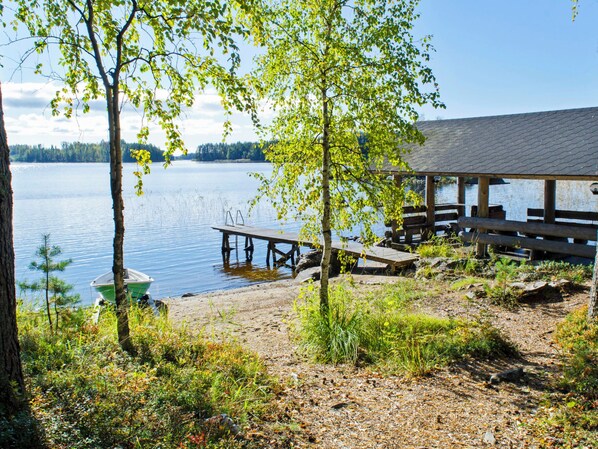 Una cabaña junto al lago con un muelle que se adentra en el agua, rodeada de árboles y vegetación.