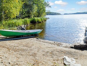 Een groene boot aan een zandstrand, aan een kalm meer met bomen op de achtergrond.