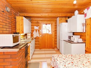 A compact kitchen with a brick wall, wooden ceiling, and white cabinets. - Suvituuli by Interhome (Liperi)