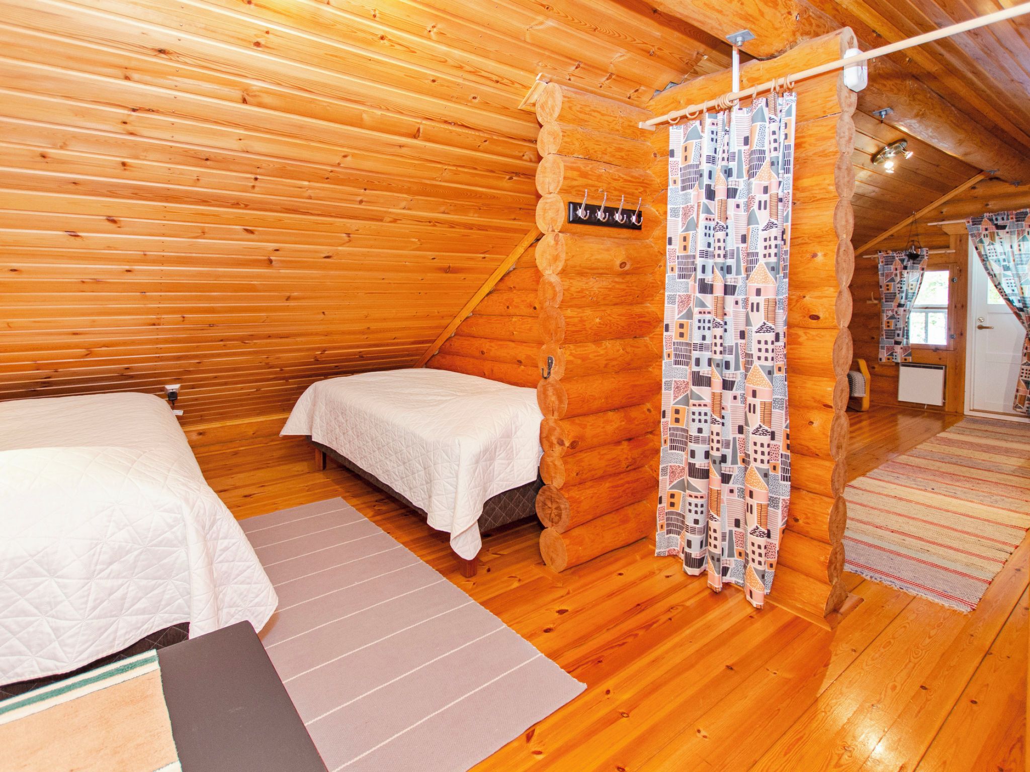Acogedor dormitorio tipo cabaña con dos camas, techo de madera y cortina estampada.