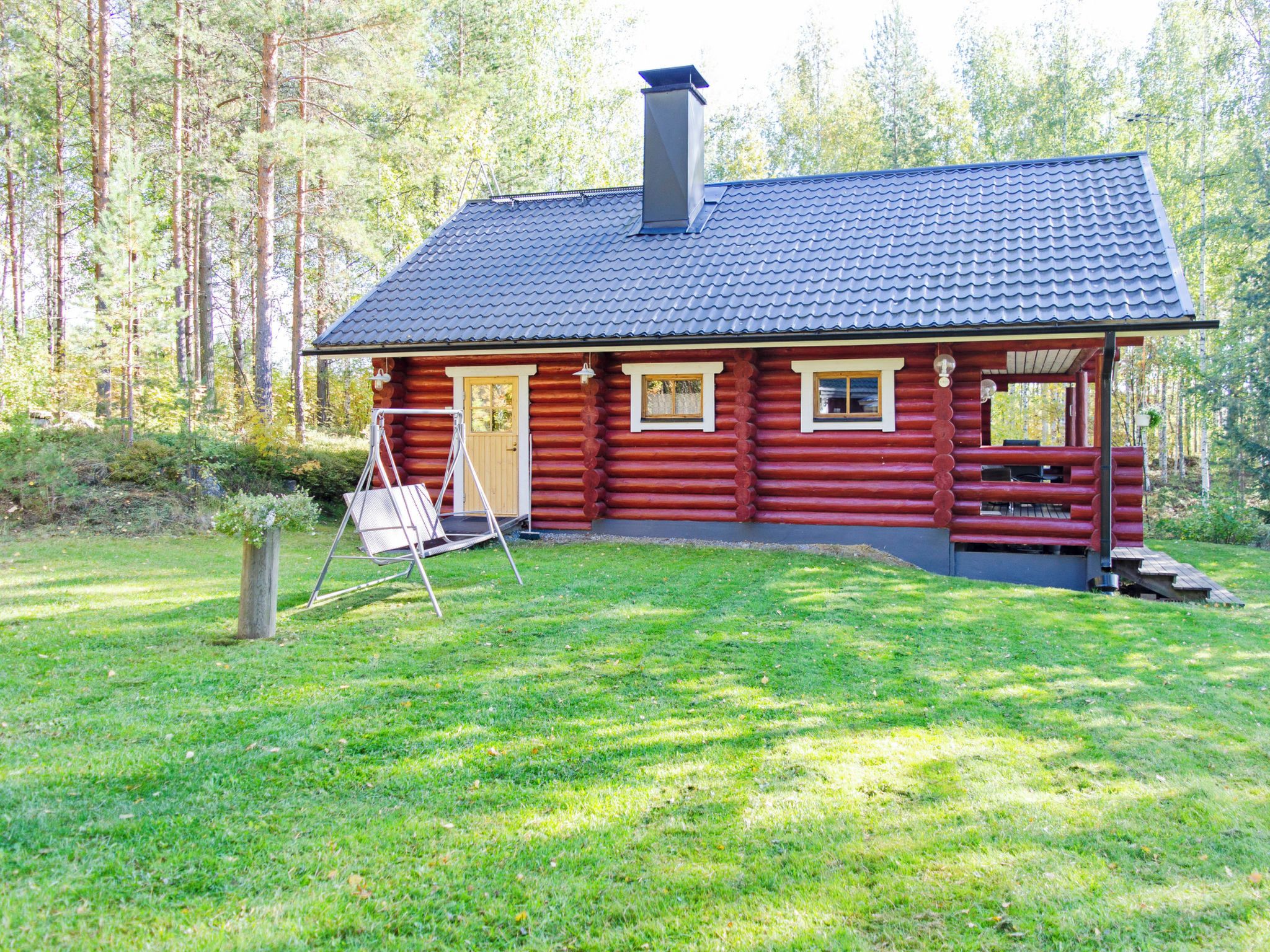Eine Blockhütte mit dunklen Ziegeldach, einem Schornstein und einer kleinen Veranda mit einer Bank.