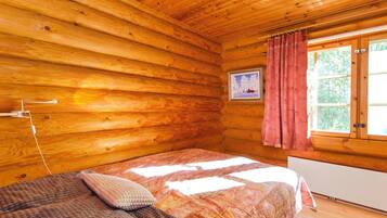 Ein Zimmer in einer Holzhütte mit einem Bett, einem Fenster mit Vorhängen und einem Bild an der Wand.