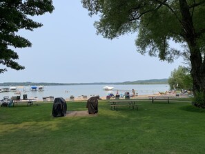 Ein Park am Seeufer mit Picknicktischen und überdachten Grillstellen, im Hintergrund liegen Boote angedockt und der See bietet einen klaren Blick.