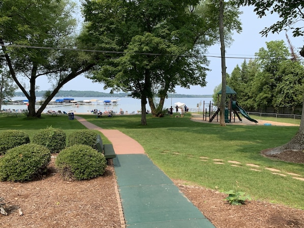 Un parque con un sendero verde, bancos y un área de juegos que incluye un tobogán.
