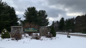 Un rètol d'entrada cobert de neu corresponent a Pinebrook, amb parets de pedra i arbres de fulles perennes.