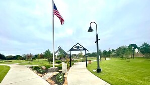 Un sentier dans un parc, avec un kiosque, un drapeau américain et un lampadaire.