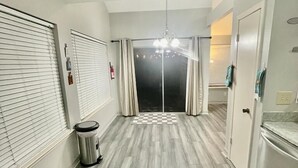 Un couloir avec un sol à carreaux, une poubelle, un luminaire au plafond et une porte donnant sur une pièce.