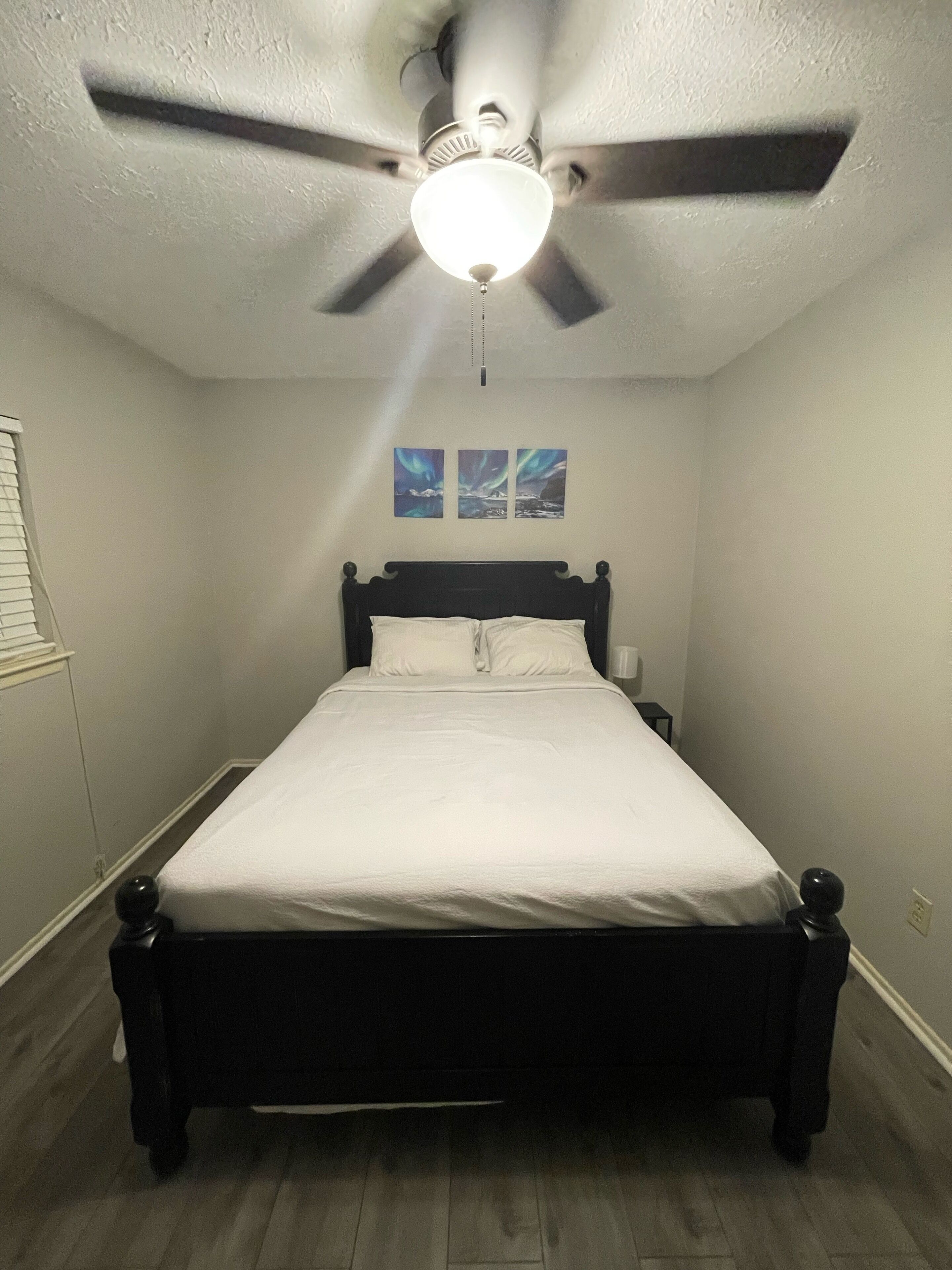 Un dormitorio con cama, ventilador de techo y dos cuadros en la pared.