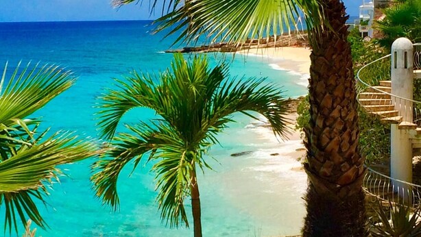 A beach with clear turquoise water, palm trees, and a stone staircase leading down to the shore. - Tranquil Oceanside: Pools & Direct Beach Access (Sint Maarten)