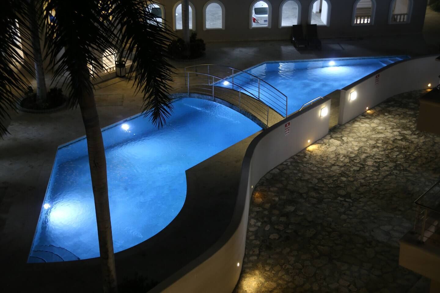 Una piscina de diseño curvo, rodeada de suelo de piedra y palmeras.