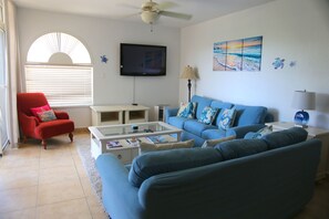 A living room with a blue sofa, a red armchair, a coffee table, a TV, and artwork on the wall.