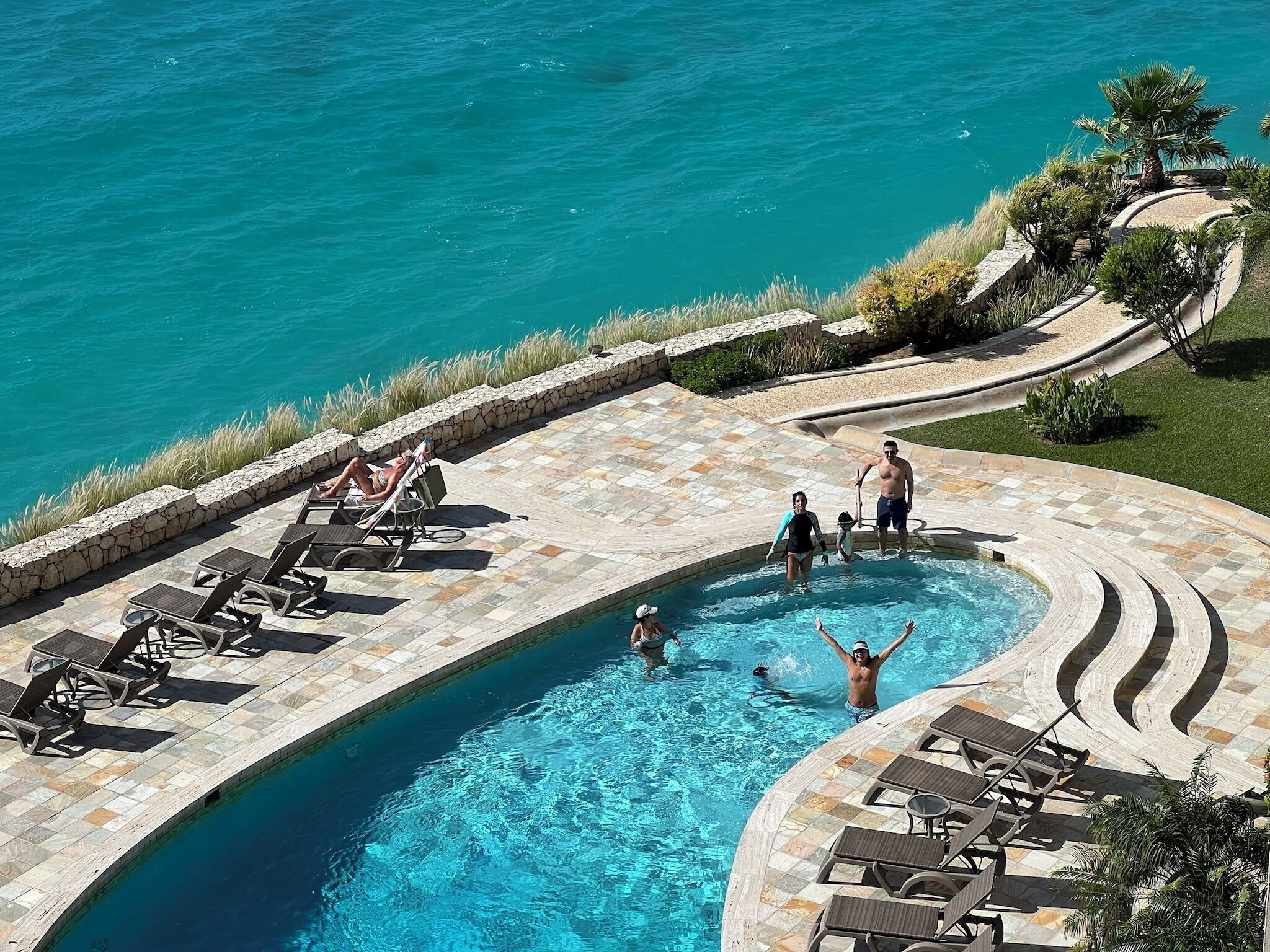 Ein Pool mit geschwungener Kante, umgeben von Liegestühlen und einer Steinterrasse.