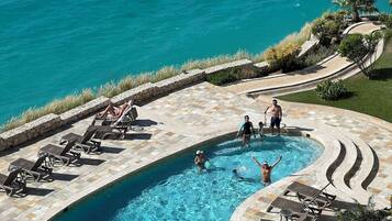Ein Pool mit geschwungener Kante, umgeben von Liegestühlen und einer Steinterrasse.