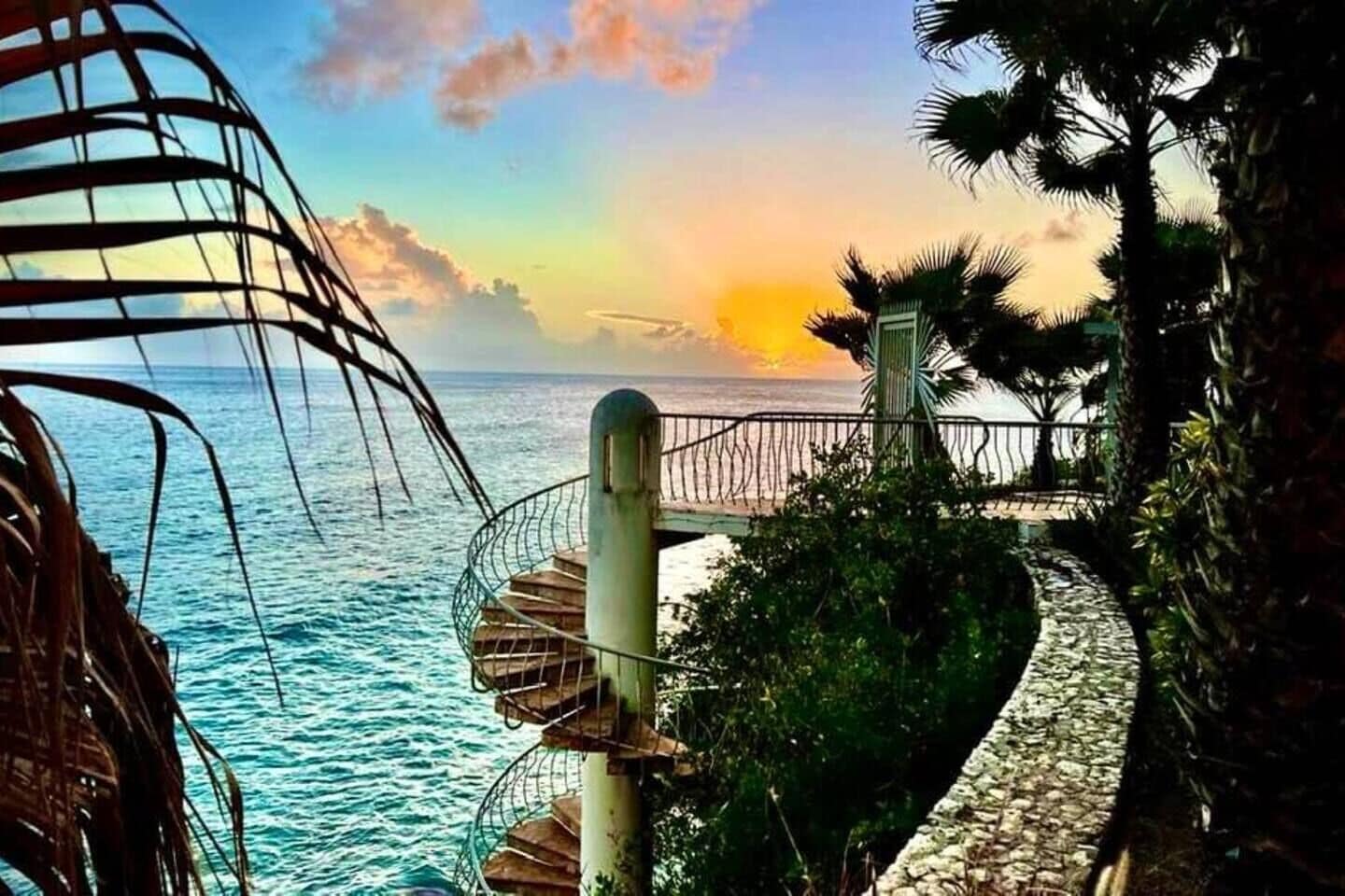 Eine Wendeltreppe führt zu einem Balkon mit Blick auf das Meer und einen Sonnenuntergang.