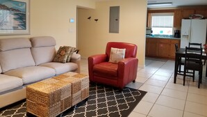A living room with a sofa, a red armchair, a woven ottoman, and a ceiling fan. - Beach-living 2 bed (Fernandina Beach)