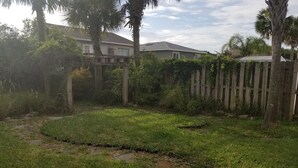 A grassy backyard with a wooden fence, trees, and a house in the background. - Beach-living 2 bed (Fernandina Beach)